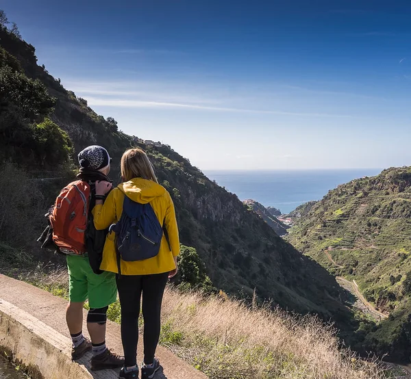Hikers with backpacks overlooking a coastal valley from a levada path