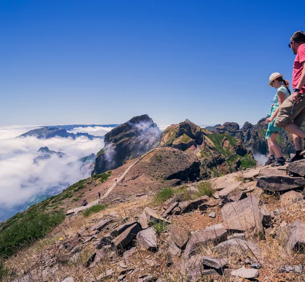 Two hikers walking along the Pico do Areeiro ridge trail above the clouds
