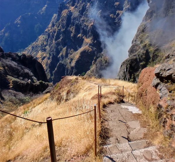 Exposed mountain trail with a rope handrail above the clouds on Madeira