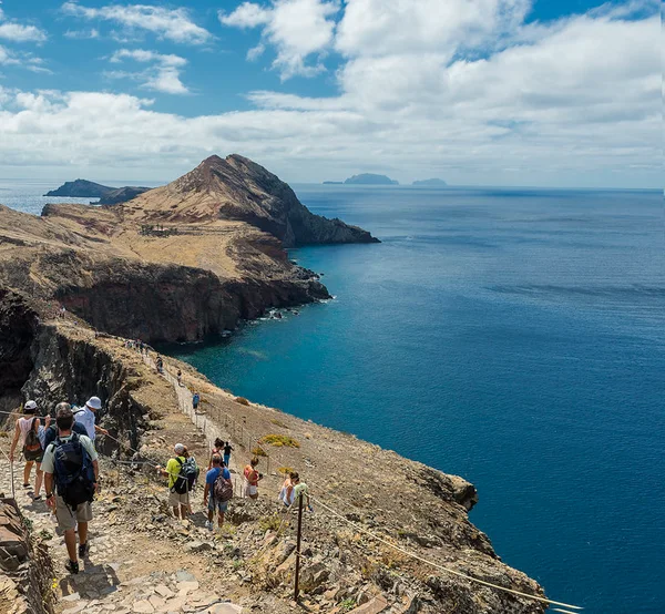 A crowd of hikers walking a popular coastal cliff trail with islets in the distance