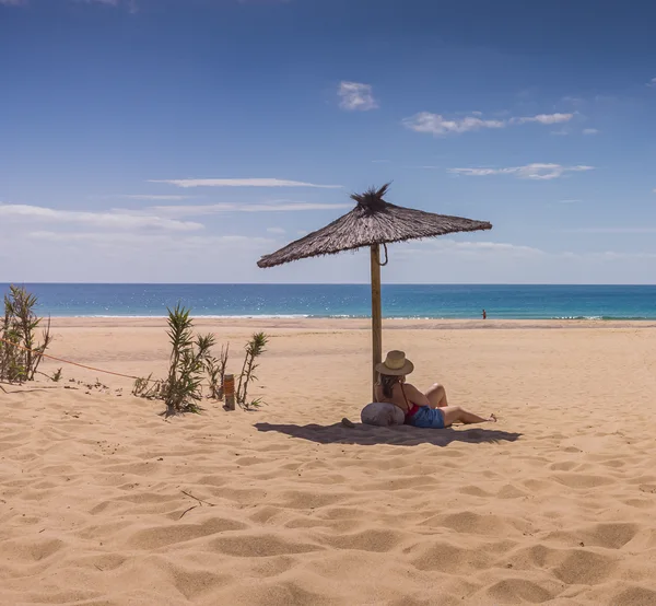 A woman relaxing alone under a straw umbrella on an empty Porto Santo beach