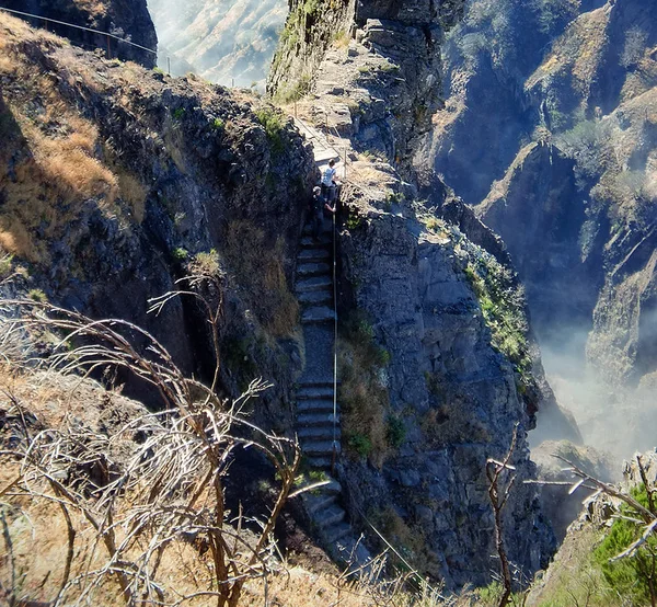 Hikers climbing a stone staircase on a narrow rocky pinnacle on the PR1 trail