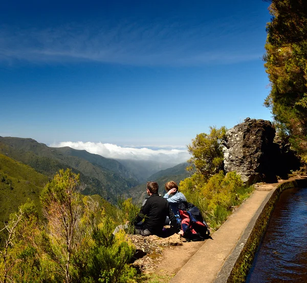 A couple resting on a levada wall overlooking a misty mountain valley