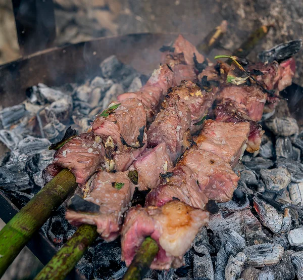 Espetada beef skewers grilling over charcoal on bay laurel sticks